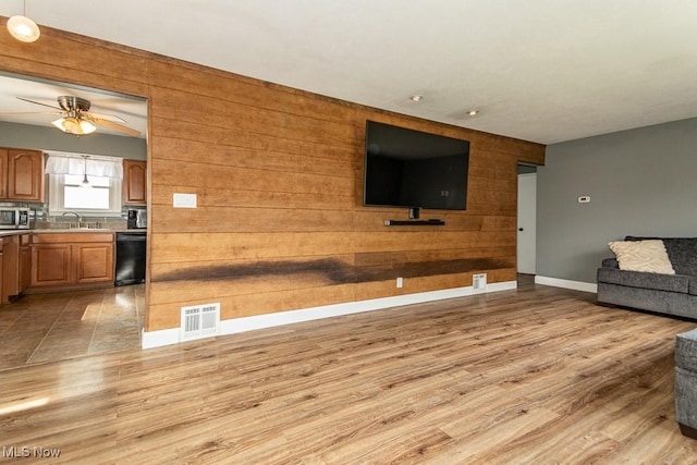 unfurnished living room featuring a ceiling fan, light wood-style flooring, baseboards, visible vents, and wood walls