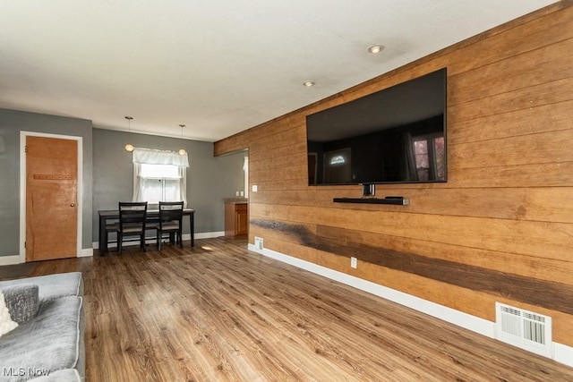 living room featuring wood finished floors, visible vents, baseboards, and wooden walls