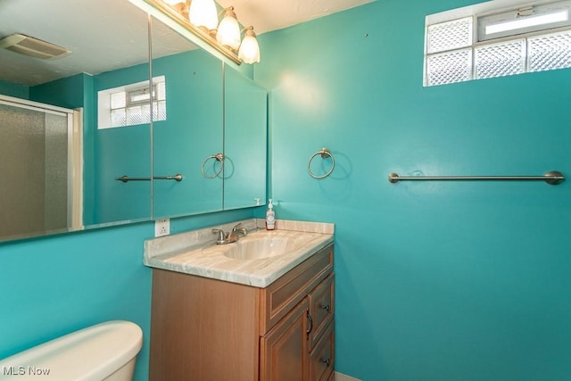 full bathroom with toilet, vanity, visible vents, and a shower stall