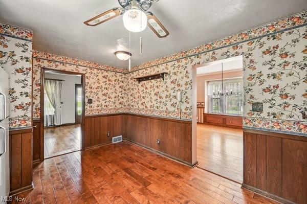 empty room with a healthy amount of sunlight, visible vents, a wainscoted wall, and hardwood / wood-style flooring