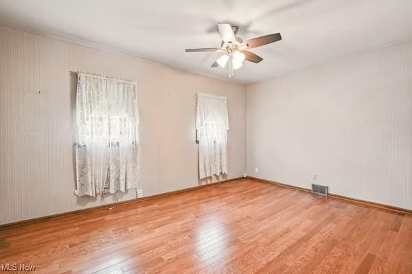 empty room featuring visible vents, a ceiling fan, plenty of natural light, and wood finished floors