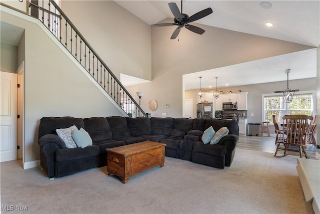 living area with a ceiling fan, stairs, light carpet, and high vaulted ceiling