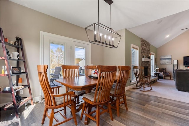 dining room featuring lofted ceiling, wood finished floors, a chandelier, baseboards, and a stone fireplace