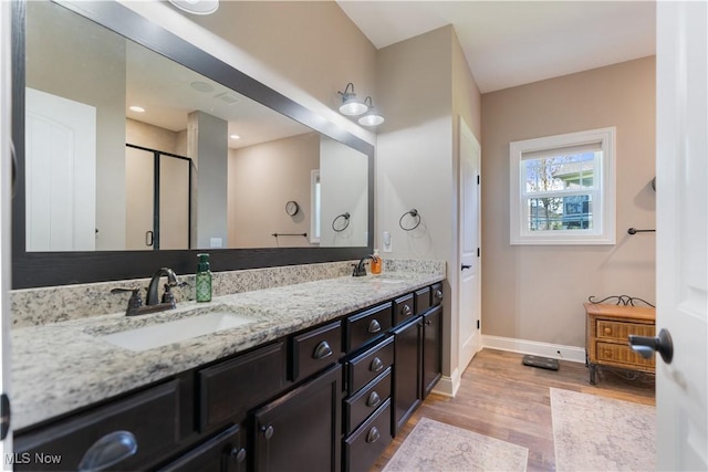 bathroom featuring baseboards, a stall shower, a sink, and wood finished floors