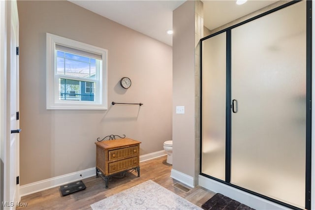 bathroom with a stall shower, toilet, baseboards, and wood finished floors