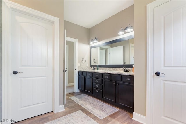 bathroom featuring a sink, double vanity, baseboards, and wood finished floors