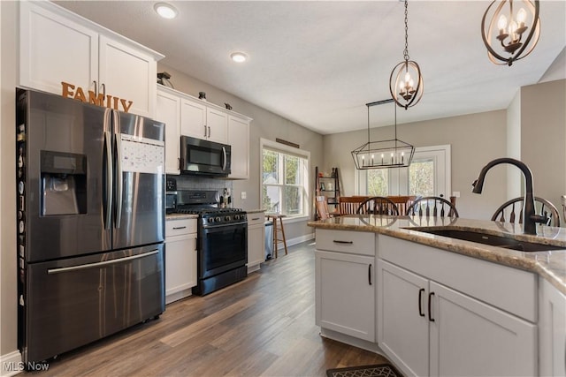 kitchen with a notable chandelier, a sink, white cabinets, appliances with stainless steel finishes, and dark wood-style floors