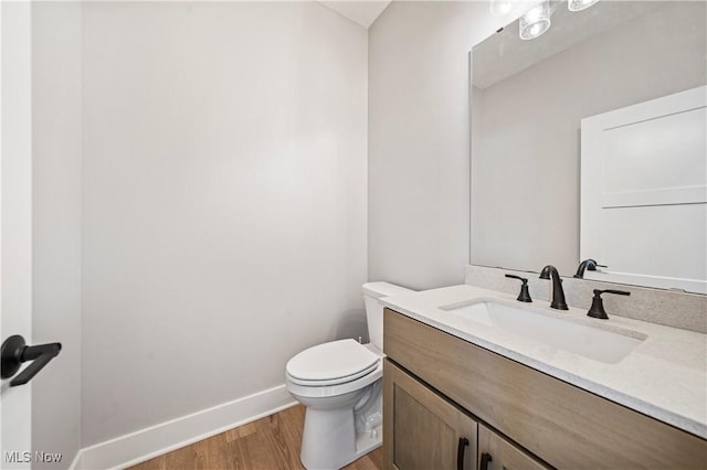 half bath featuring vanity, toilet, baseboards, and wood finished floors