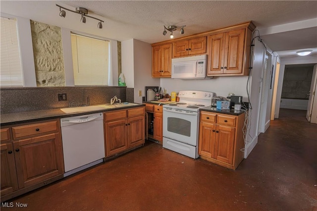 kitchen with a sink, white appliances, rail lighting, finished concrete floors, and dark countertops