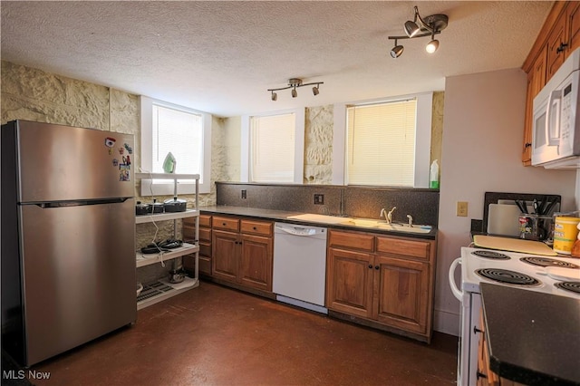 kitchen featuring a textured ceiling, brown cabinetry, white appliances, a sink, and concrete flooring