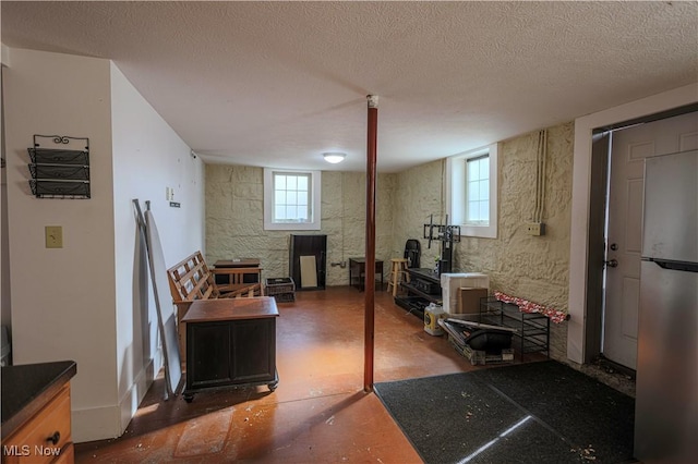 below grade area with freestanding refrigerator, a textured ceiling, and a healthy amount of sunlight