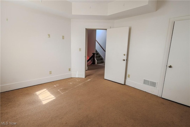 unfurnished room with a tray ceiling, baseboards, carpet flooring, visible vents, and stairs