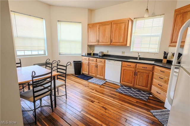 kitchen with dark countertops, dark wood finished floors, a sink, and white appliances
