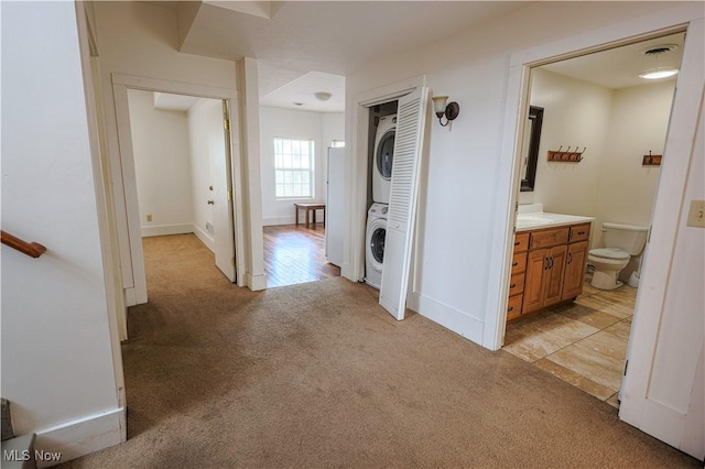 hallway with baseboards, visible vents, stacked washer / dryer, and light colored carpet