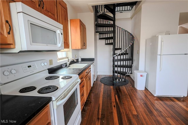 kitchen with brown cabinetry, white appliances, a sink, dark countertops, and dark wood-style floors