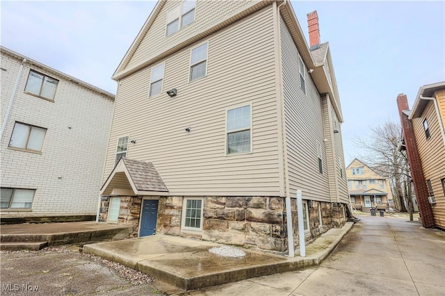 back of property featuring stone siding and a chimney