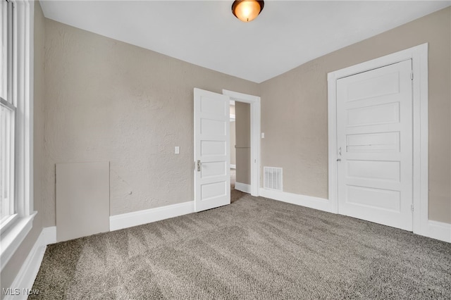 unfurnished bedroom featuring a textured wall, visible vents, baseboards, and carpet floors