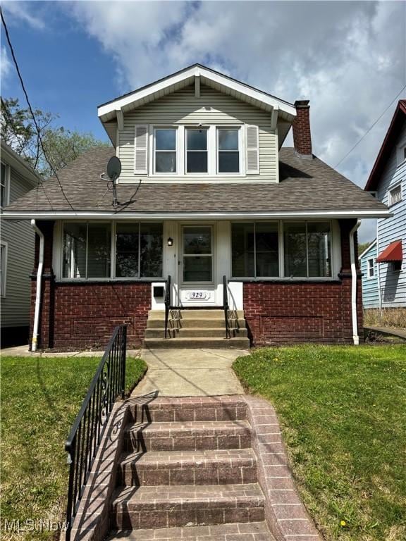 view of front of home with a chimney, entry steps, brick siding, and a front lawn