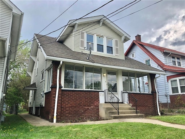 bungalow-style house featuring entry steps, a shingled roof, brick siding, and a front yard