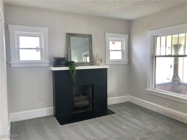 unfurnished living room featuring a textured ceiling, visible vents, carpet flooring, baseboards, and a fireplace with flush hearth