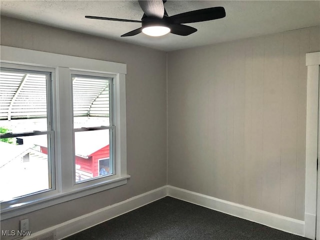 unfurnished room featuring baseboards, a ceiling fan, plenty of natural light, and dark carpet