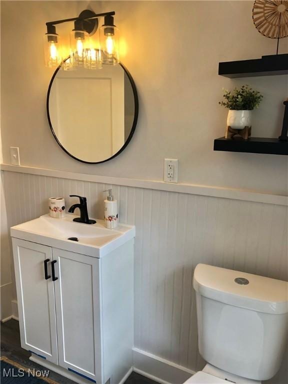 half bathroom with a wainscoted wall, toilet, wood finished floors, and vanity