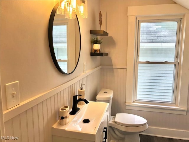 half bathroom with wainscoting, vanity, toilet, and a notable chandelier