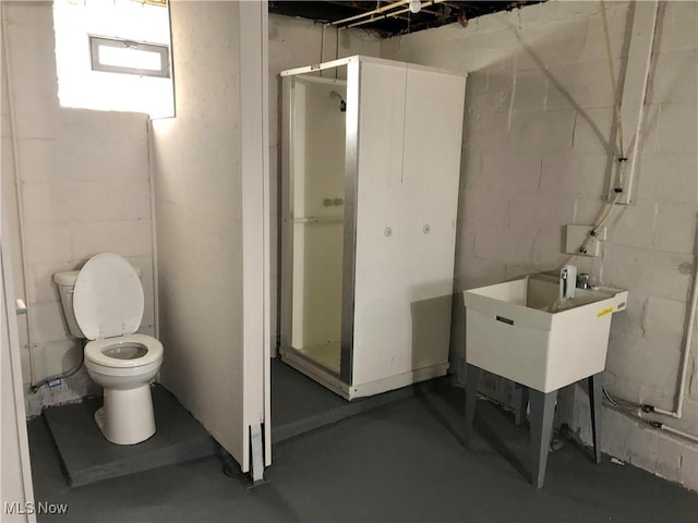 bathroom featuring finished concrete floors, toilet, concrete block wall, and a stall shower
