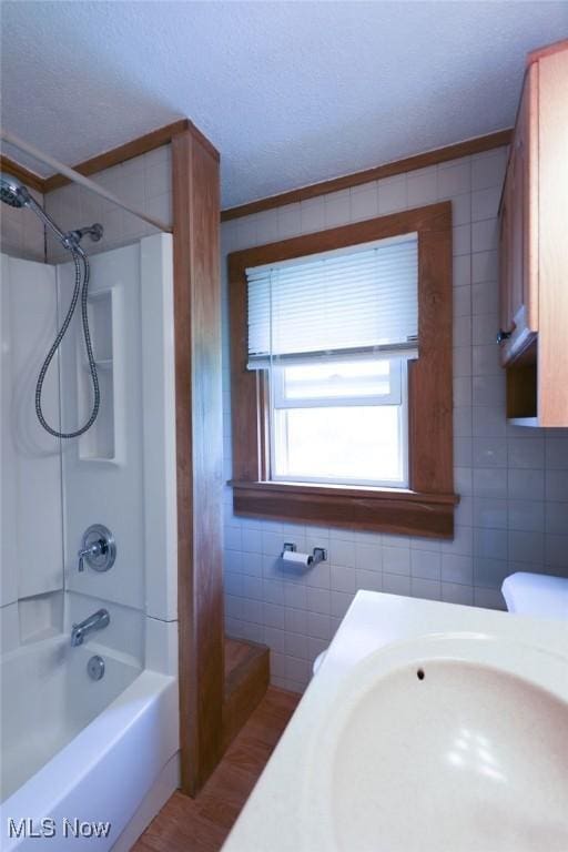bathroom with tile walls, a textured ceiling, a sink, bathtub / shower combination, and wood finished floors