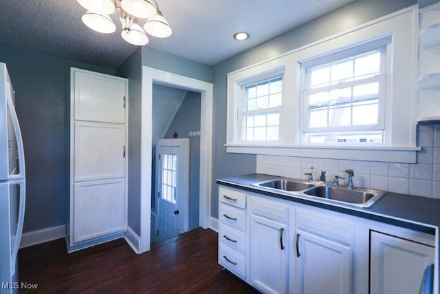 kitchen featuring a sink, tasteful backsplash, freestanding refrigerator, dark wood-type flooring, and baseboards