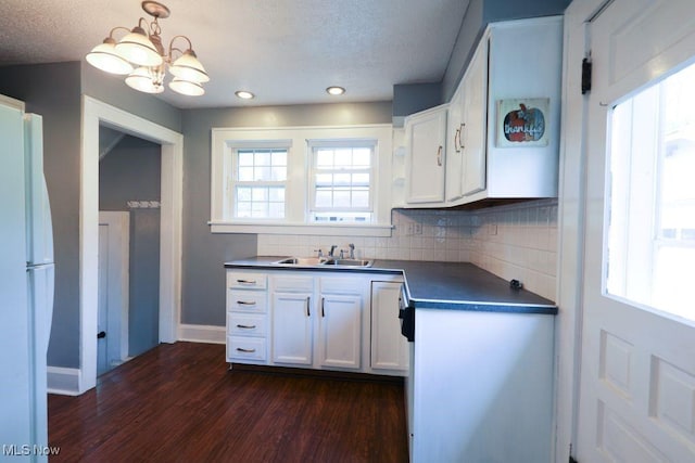 kitchen with freestanding refrigerator, baseboards, an inviting chandelier, a sink, and dark countertops