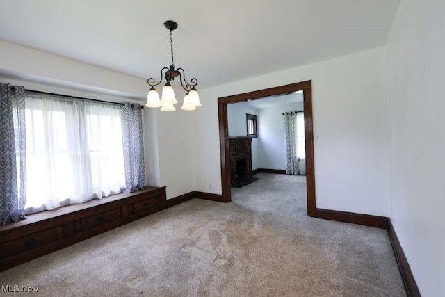 empty room featuring a fireplace, carpet, a notable chandelier, and baseboards