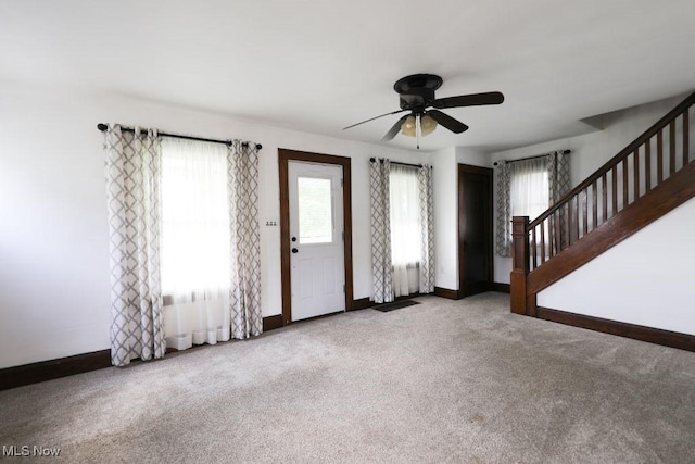 unfurnished living room with baseboards, stairs, a ceiling fan, and carpet floors