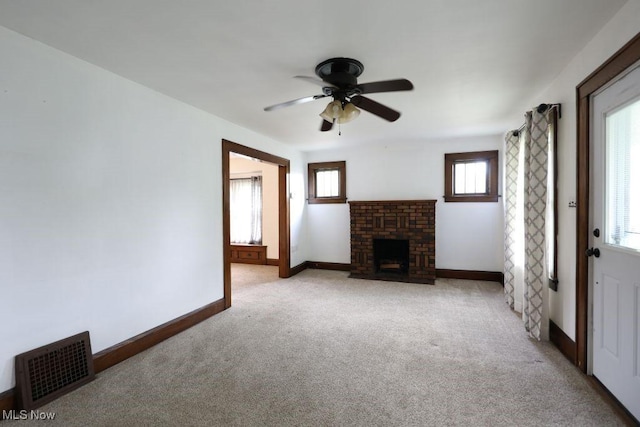 unfurnished living room with light colored carpet, visible vents, a fireplace, ceiling fan, and baseboards