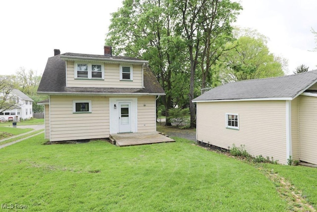 back of house with a shingled roof, a chimney, and a lawn
