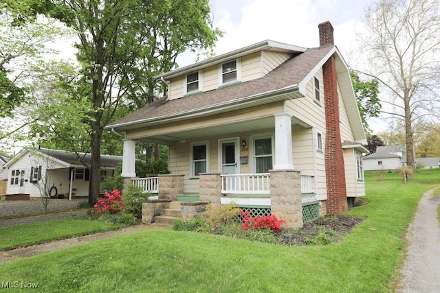 view of front facade featuring covered porch, roof with shingles, a chimney, and a front yard