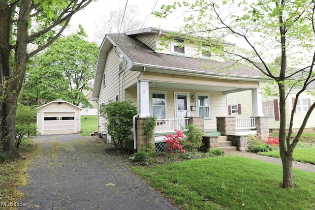 view of front of home with covered porch, aphalt driveway, an outbuilding, roof with shingles, and a detached garage
