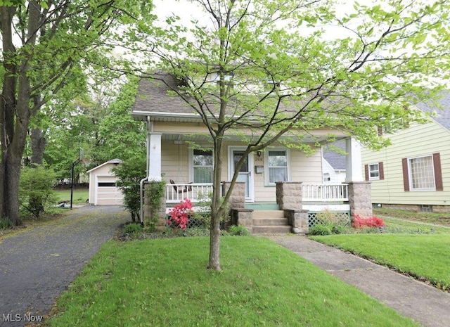 view of front facade featuring covered porch, a detached garage, a front lawn, and an outbuilding