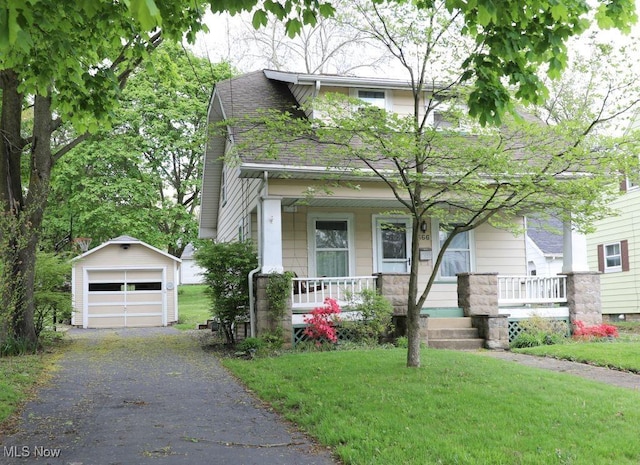view of front of house featuring covered porch, a garage, a front lawn, an outdoor structure, and roof with shingles