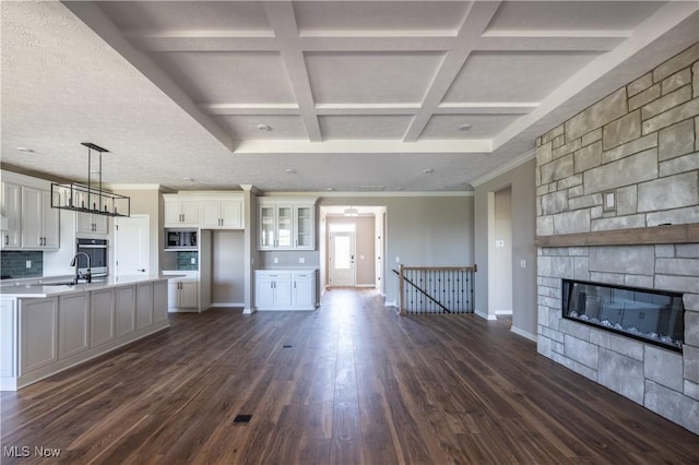unfurnished living room with dark wood-type flooring, a fireplace, beamed ceiling, coffered ceiling, and baseboards