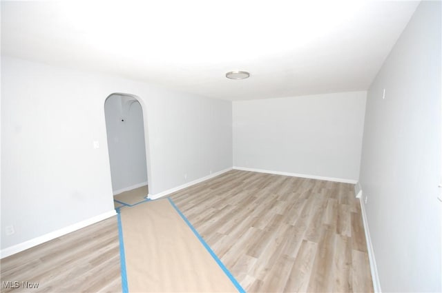 unfurnished room with arched walkways, light wood-style floors, and baseboards