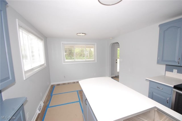 kitchen with range, visible vents, blue cabinets, arched walkways, and light countertops