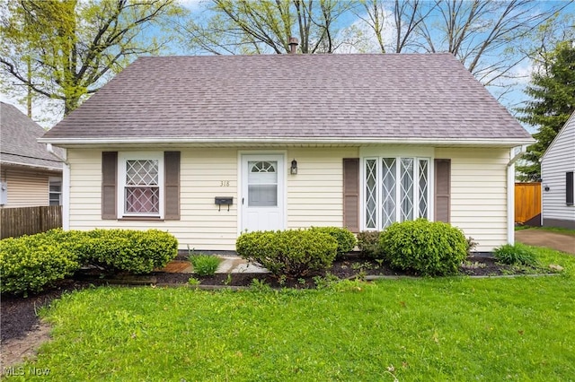 view of front of property featuring a front lawn, a shingled roof, and fence