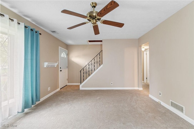 carpeted empty room featuring stairs, baseboards, a ceiling fan, and visible vents