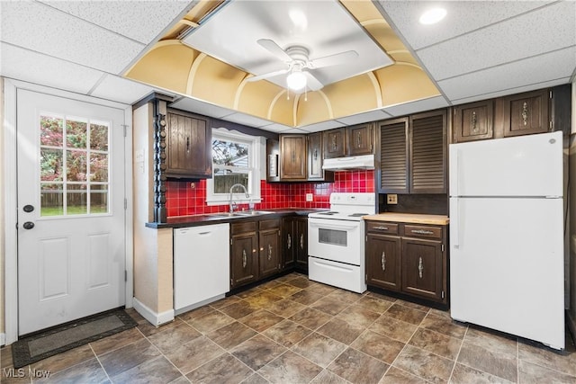 kitchen with a sink, dark countertops, ceiling fan, white appliances, and tasteful backsplash