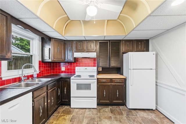 kitchen featuring under cabinet range hood, dark countertops, a sink, and white appliances