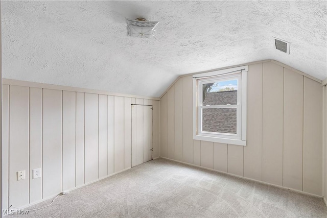 bonus room featuring a decorative wall, a textured ceiling, visible vents, vaulted ceiling, and carpet flooring
