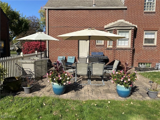 rear view of house with a patio, brick siding, a shingled roof, and fence