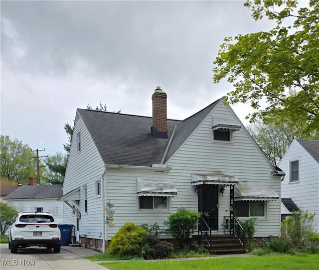view of front of home featuring a shingled roof, a chimney, and a front lawn