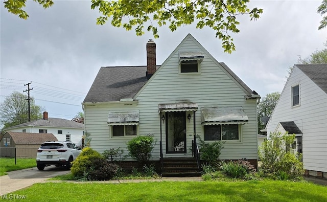 view of front of home featuring entry steps, a shingled roof, a front lawn, and a chimney